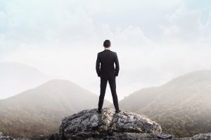 Business man standing on the top of the mountain looking at the valley. Business success concept