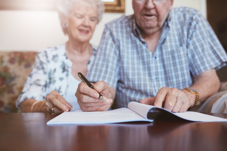 Senior couple signing will documents. Elderly caucasian man and woman sitting at home and signing some paperwork focus on hands.